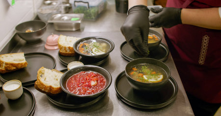 Serving meal. Kitchen process. Cafeteria chef garnishing hot dish with chopped fresh herbs. Hands adding aroma greens in soup borsch.の写真素材