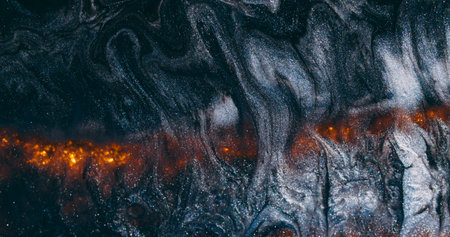 Glitter wave. Paint lava. Black ash shimmering emulsion spill on wet gray background. Hot orange glow line abstract blur volcanic.の写真素材