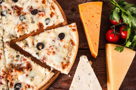 Appetizing hot pizza served on rustic wooden table with cheese assortment, parsley and cherry tomatoes, flat lay. Traditional italian cuisine.の写真素材