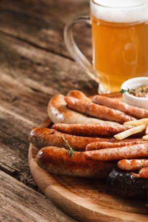 German food, Oktoberfest menu. Mug of cold light beer and wooden platter with various grilled sausages, close up view. Restaurant photo, free spaceの写真素材