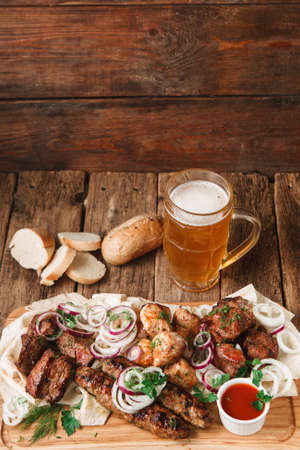 Appetizing meal in pub with fresh grilled meat assortment, pita bread, buns, and mug of cold light beer served on rustic wooden background, free spaceの写真素材