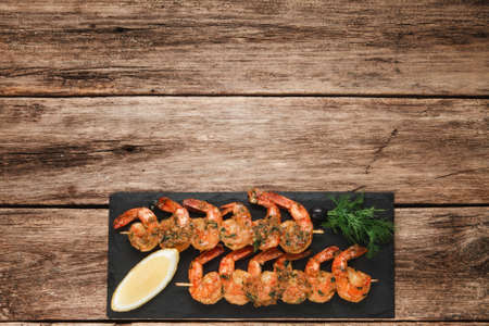 Appetizing shrimps served on black slate, flat lay. Wooden rustic table background with copy space for text. Japanese seafood, mediterranean cuisine conceptの写真素材