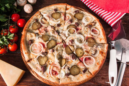 Italian hot pizza with mushrooms, onion, pickles, cheese and ham, sliced and served on wooden background with ingredients and special knife, flat lay. Restaurant menu photo.の写真素材