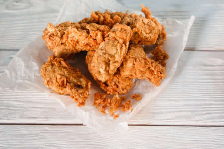 Fresh deep fried chicken in paper on white wooden table, flat lay. American cuisine, junk food, bad habits, calories, cholesterol, fatness.の写真素材