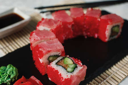 Appetizing sushi roll set served on black slate with ginger and wasabi in luxury restaurant, on straw mat background. Uramaki, Japanese healthy seafood.の写真素材