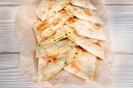 Appetizing lavash envelopes with cheese and green on white wooden table, flat lay. Pita bread, snack, fast food. Armenian and georgian national cuisine.の写真素材
