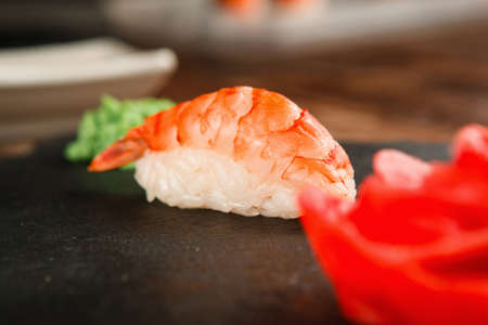 One appetizing shrimp sushi nigiri with fresh prawn served on black slate with wasabi and ginger, closeup view. Japanese national food.の写真素材