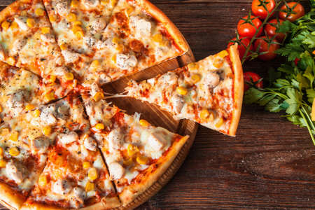 Hot delicious pizza with chicken, cheese and corn with cut piece served on rustic wooden table with ingredients, flat lay. Italian food.の写真素材