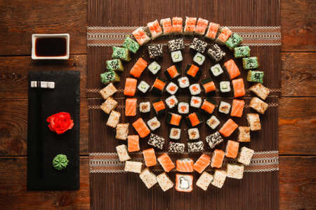 Food art, great sushi set. Appetizing assortment of rolls, colorful round ornament served on brown straw mat, flat lay. Luxury japanese restaurant menu photo.の写真素材