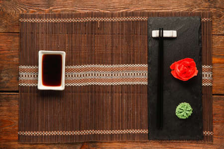 Japanese food background, table served for sushi, flat lay. Empty straw mat with soy sauce and black slate with chopsticks, wasabi and ginger.の写真素材