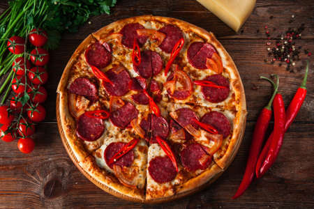 Appetizing italian food. Pizza with cherry tomatoes, sausage, chili pepper and cheese with ingredients on rustic wooden background, flat lay.の写真素材