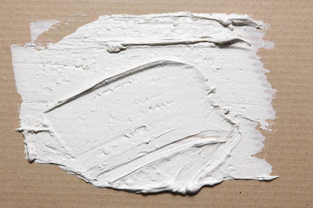 White stucco smeared on grey cardboard with spatula, rough texture, closeup. Building, construction, material sample, plaster backgroundの写真素材