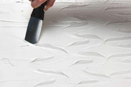 Unrecognizable person with spatula make texture on wet white plaster. Hand with pallet work with stucco, closeup. Constructional background with free space.の写真素材