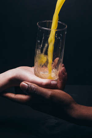 Hands hold glass, pouring fresh orange juice on black background. Healthy life, vegetarian, spirit, full of energy, international couple concept.の写真素材