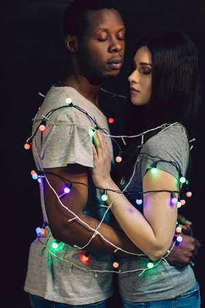 Couple in love tied together with sparkling garland. Black man and white woman, togetherness, unity...