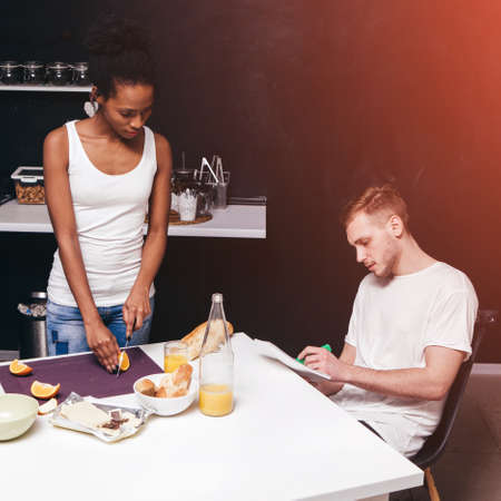 Family everyday life and values. A young interracial couple in the kitchen in a domestic setting is preparing a healthy meal together. Modern interior in the background with a free spaceの写真素材