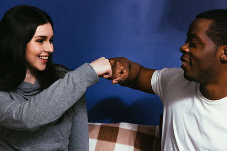 Young couple of black man and white woman on couch, closeup. Fist bump, togetherness, smile, joy,...