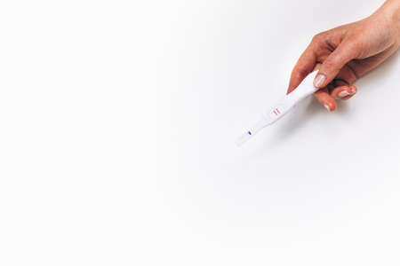 Pregnancy positive test in female hand, flat lay white background with free space. In vitro fertilization success, pregnant woman, happy maternity concept.の写真素材