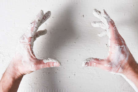 Repair background. Worker dirty hands hold something on white plaster surface, flat lay, void....
