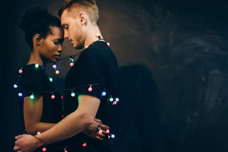 Tender love and happy relationships in the New Years holiday. Young interethnic couple on a black background with free spaceの写真素材