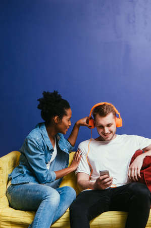 Young interracial couple in quarrel at home, white man ignore black woman. Wear headphones and look...