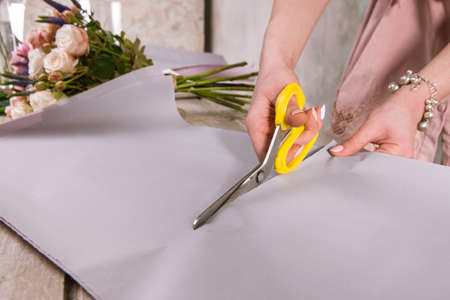 Florist wrapping bouquet of rose flowers closeup. The decorator works in a greenhouse with a pink bouquet. Floristic workshop, skill, decor, small business conceptの写真素材