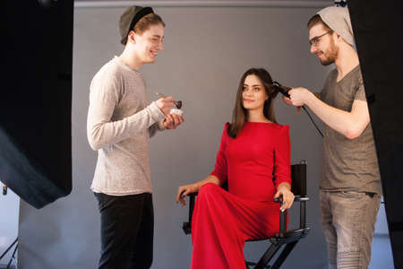 Hairdresser and make-up artist work together in studio . Men doing makeup and hairstyle for woman. Creative team make commercials. Photo school, lookbook, fashion backstage conceptの写真素材