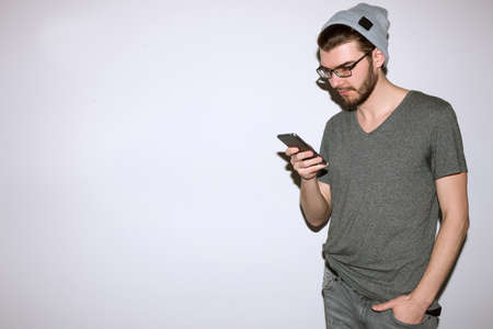 Hipster read text message on phone. Communication, friendship, social network concept. Man in gray casual cloth standing on white background with smartphoneの写真素材