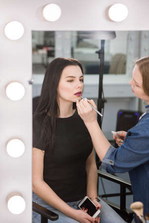 Reflection of makeup artist putting lipstick on woman. Beautician applying makeup in salonの写真素材
