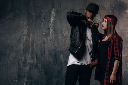 Gang members couple with gun. Criminal teenagers on dark background. Love and romance in outlaw familyの写真素材