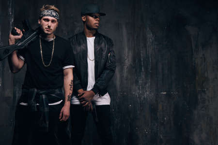 Group of young criminals with guns. Armed band of gangsters with tattoo and weapon on dark background. Outlaw, ghetto, murderer, robbery conceptの写真素材