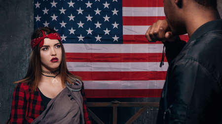 Quarrel in american family. Black man and caucasian woman with little baby on US national flag background. Social problem, child custody, youth pregnancy conceptの写真素材