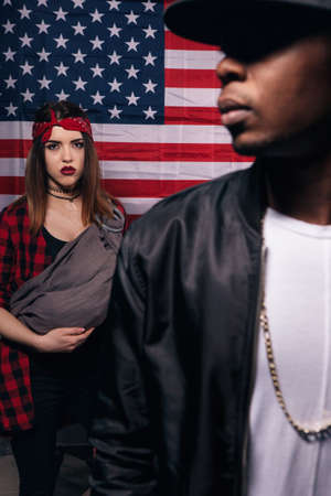 Quarrel in american family. Black man and caucasian woman with little baby on US national flag background. Social problem, child custody, youth pregnancy conceptの写真素材