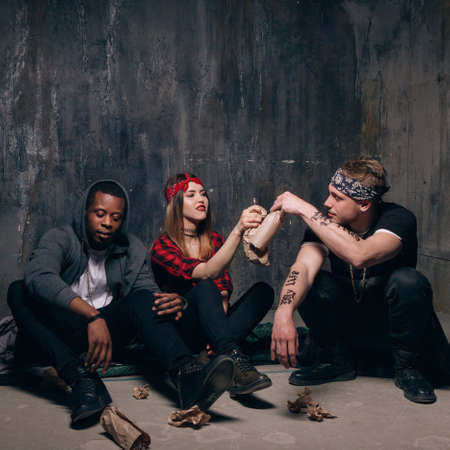 Group of alcoholic young people make cheers at gung members party. Youth addiction problem. Laughing drunk caucasian girl holding alcohol bottle, two guys with tattoo sits near .の写真素材