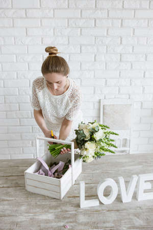 Decorator make flower bouquet. Young girl makes an ornament from white flowers in a workshop. Light florist studio with brick wall on background.の写真素材