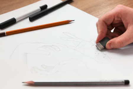 From above hand erasing lines on a sketch. Horizontal indoors shot. Drawing lessons, art school, young artist conceptの写真素材