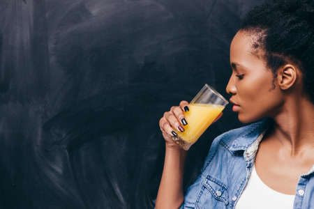Young african woman drink glass of orange juice. Healthy life, detox vitamin diet, vegetarian concept.の写真素材