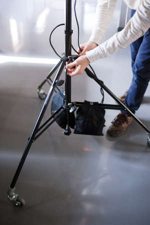 Unrecognizable man setting the photo tripod. Assistant work with equipment in photostudio....