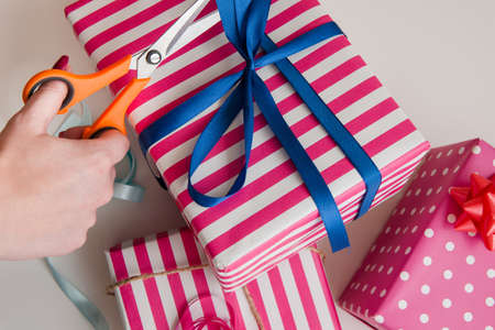 Pink gift wrapping. Birthday background. Hands packing festive boxes with blue ribbon.の写真素材