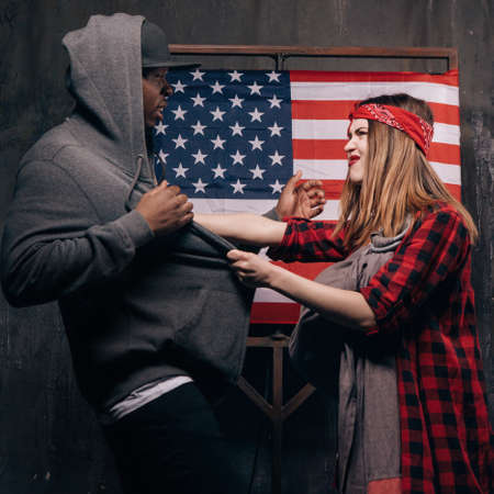 Jealousy in the US family. Conflict in couple. Angry wife and husband on USA national flag background. Divorce, social problem, home violence, youth pregnancy conceptの写真素材