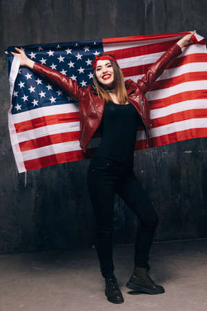 Happy smiling girl with USA flag behind the back on dark background. American patriot, national event celebration, pride, us citizen conceptの写真素材