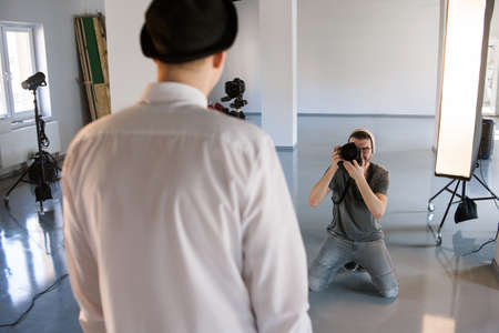 Back view of a male model posing for professional photographer in studio. POV of model during photoshooting. Fashion photo session backstageの写真素材