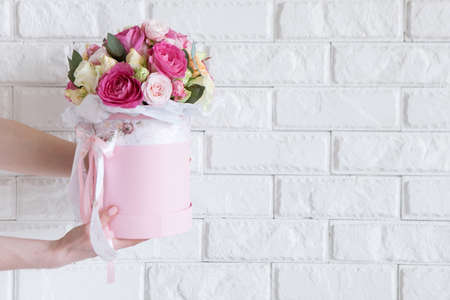 Female hand gives bunch with pink and yellow roses on white brick background. Gift for mother or woman, florist work, wedding decor, beautiful bouquet sale conceptの写真素材