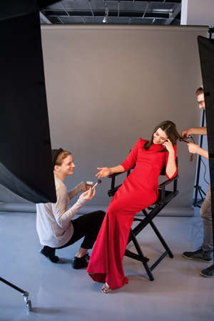 Happy beautician team on photoshoot. Hairdresser and make-up artist work together in studio . Creative people make commercials. Photo school, fashion backstage conceptの写真素材