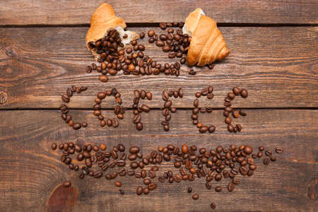 Roasted coffee beans in croissant on wooden background. Closeup of seed filling on dark brown table. Top view. Extra energy conceptの写真素材