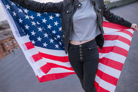 Unrecognizable girl with USA flag behind the back on city background. Patriot, national event...