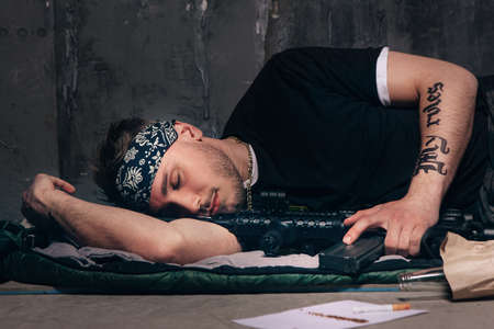 Mercenary sleeping with a rifle. Bad habits. Cigarette, alcohol, weapon top view. Careless lifestyle, gang war, social problem, negative addiction conceptの写真素材