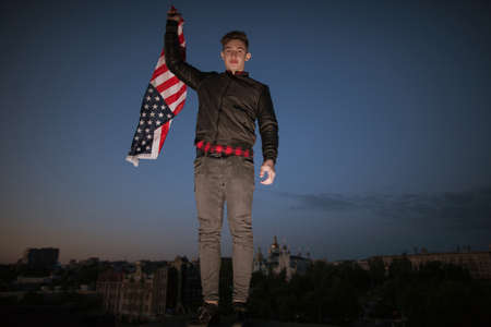 Guy with US flying flag at night city. Proud american patriot celebrate national event. Teenager on...