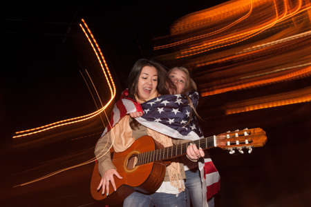 Students celebrate Independence Day at night. Singer with guitar and happy girl with american flag...