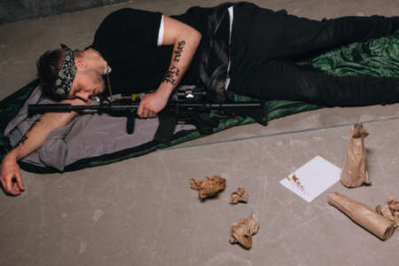Gangster sleep with rifle. Bad habits. Cigarette, alcohol, weapon top view. Careless lifestyle, gang war, social problem, negative addiction conceptの写真素材